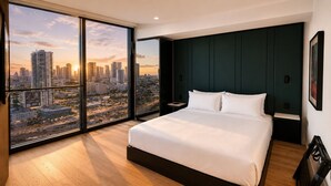 Un dormitorio con una cama grande, una mesita de noche, vistas de un paisaje urbano a través de ventanas del suelo al techo, y una pared de acento en color verde oscuro.