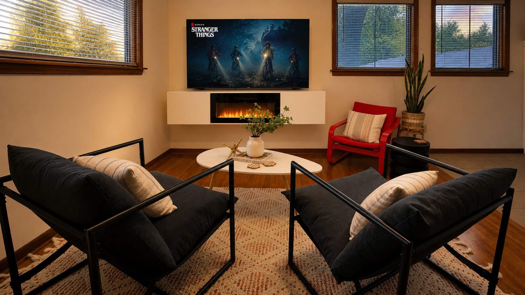 Una sala de estar con chimenea, dos sillones, una silla roja y un televisor de pantalla plana mostrando 'Stranger Things'.