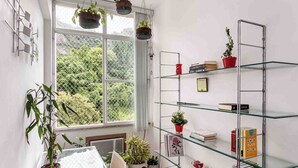 A room with a large window, a glass table, and shelves with books and plants. - Boutique Apartment | 5 min from Copacabana Beach and Metro | Restaurants, Bars and Shops (Rio de Janeiro)
