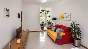 A modern living room with a red sofa, a TV, and a dining area with a table and chairs. - Boutique Apartment | 5 min from Copacabana Beach and Metro | Restaurants, Bars and Shops (Rio de Janeiro)