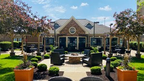 An outdoor patio area with seating, a fire pit, and a building with large windows and a stone facade.