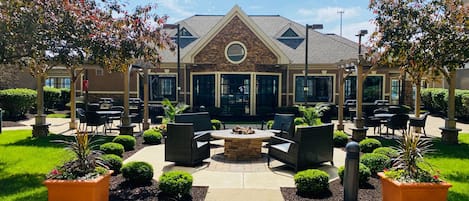 An outdoor patio area with seating, a fire pit, and a building with large windows and a stone facade.