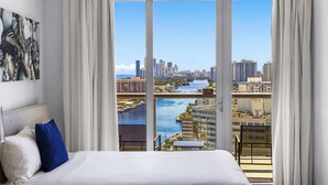 A hotel room with a large bed, a view of a cityscape, and a balcony with a railing. - Ocean & Canal View Studio with Balcony Beachwalk Resort 2109 (Hallandale Beach)