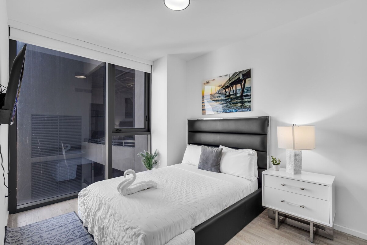 A modern bedroom with a bed, a nightstand, a lamp, and a painting on the wall.