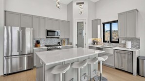 Una cocina moderna con electrodomésticos de acero inoxidable, una isla central con taburetes y vistas por una ventana.