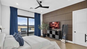Un dormitorio moderno con una cama grande, ventilador de techo, televisión y vista al desierto.