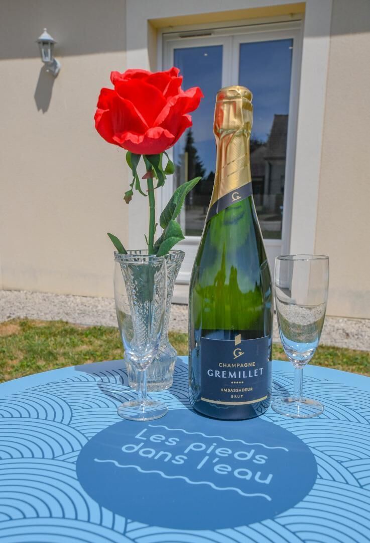 Una botella de champán, una copa y un jarrón con una rosa roja sobre una mesa con estampado azul.