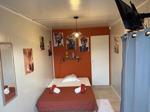 A bedroom with a bed, a mirror, artwork on the walls, a shelf with items, and a door. - Unique Bungalow for 2 People in KA CLAUDINE, SAINT FRANÇOIS (Saint-François)