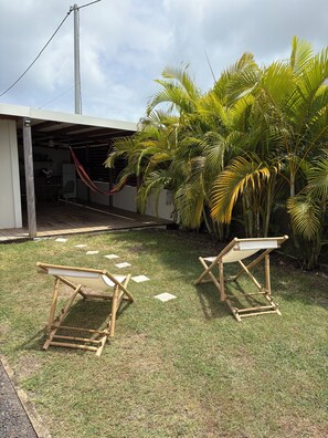A backyard with a hammock, palm trees, and two wooden chairs. - Unique Bungalow for 2 People in KA CLAUDINE, SAINT FRANÇOIS (Saint-François)