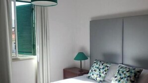 A hotel room with a bed, a bedside lamp, and a window with curtains. - Funchal Petrolhead Apartment (Funchal)