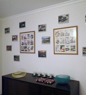 Ein Zimmer mit einem dunklen Holztisch, einer petrolfarbenen Schale und einer gerahmten Collage von Bildern an der Wand.