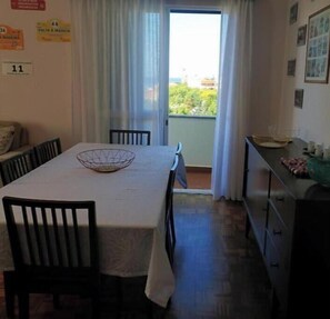 Ein Zimmer mit Esstisch, Stühlen, einem Fenster mit Vorhängen, einem Schminktisch und Blick auf Grünfläche.