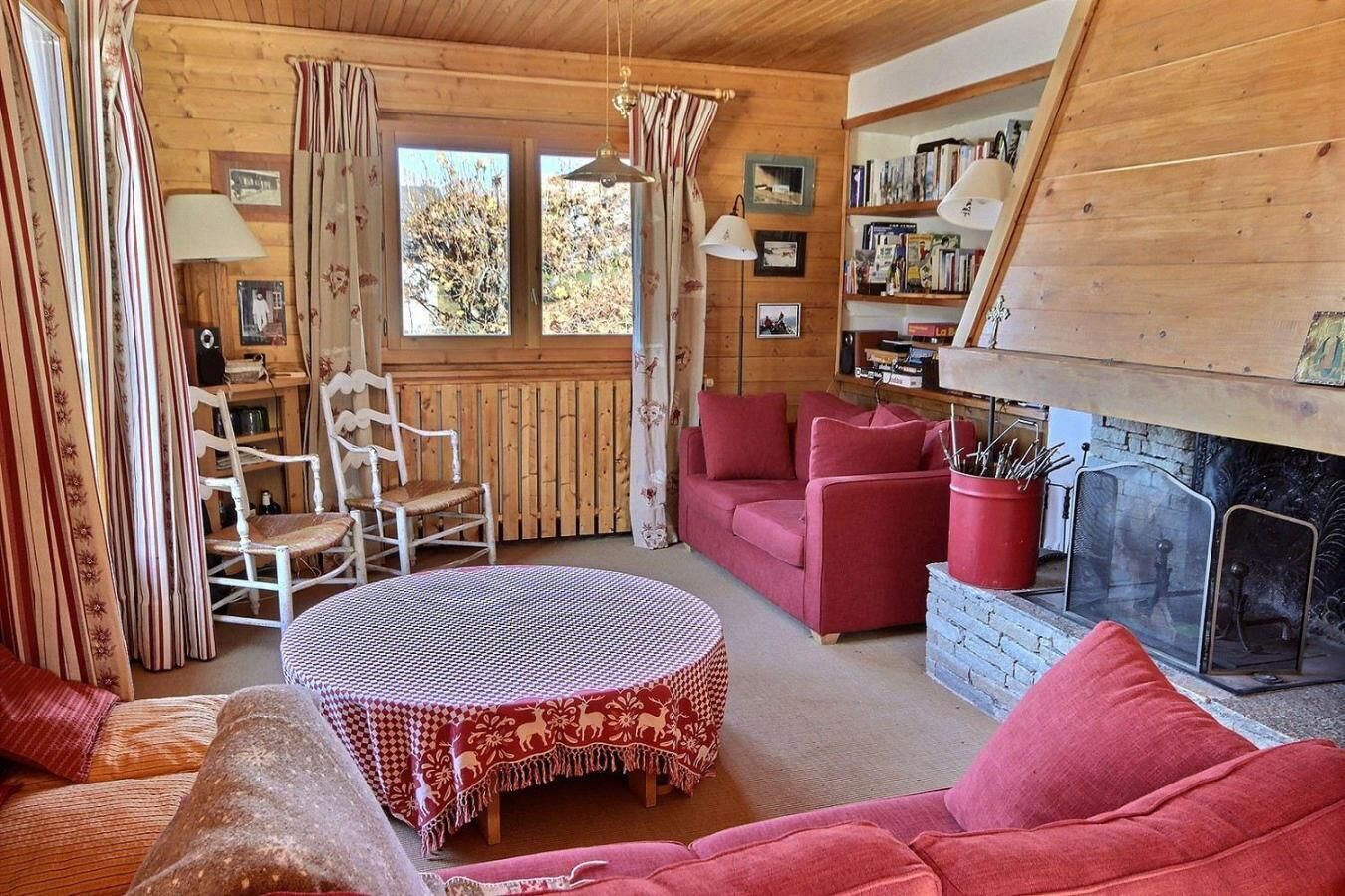 Una habitación acogedora con chimenea, una mesa redonda, un sofá rojo y una estantería.