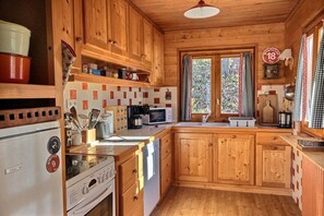 Eine Holzhütte mit einer Küche, inklusive Kühlschrank, Herd, Mikrowelle und Holzschränken.