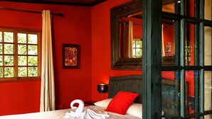A room with a bed, a window with curtains, a nightstand, and a wall-mounted lamp.