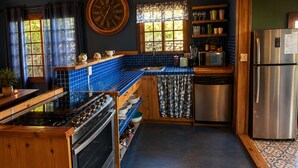 A kitchen with wooden cabinets, a blue tiled backsplash, a stainless steel refrigerator, and a clock on the wall.