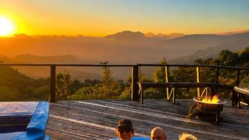 Un bain à remous sur une terrasse en bois, avec vue sur les montagnes au coucher du soleil.