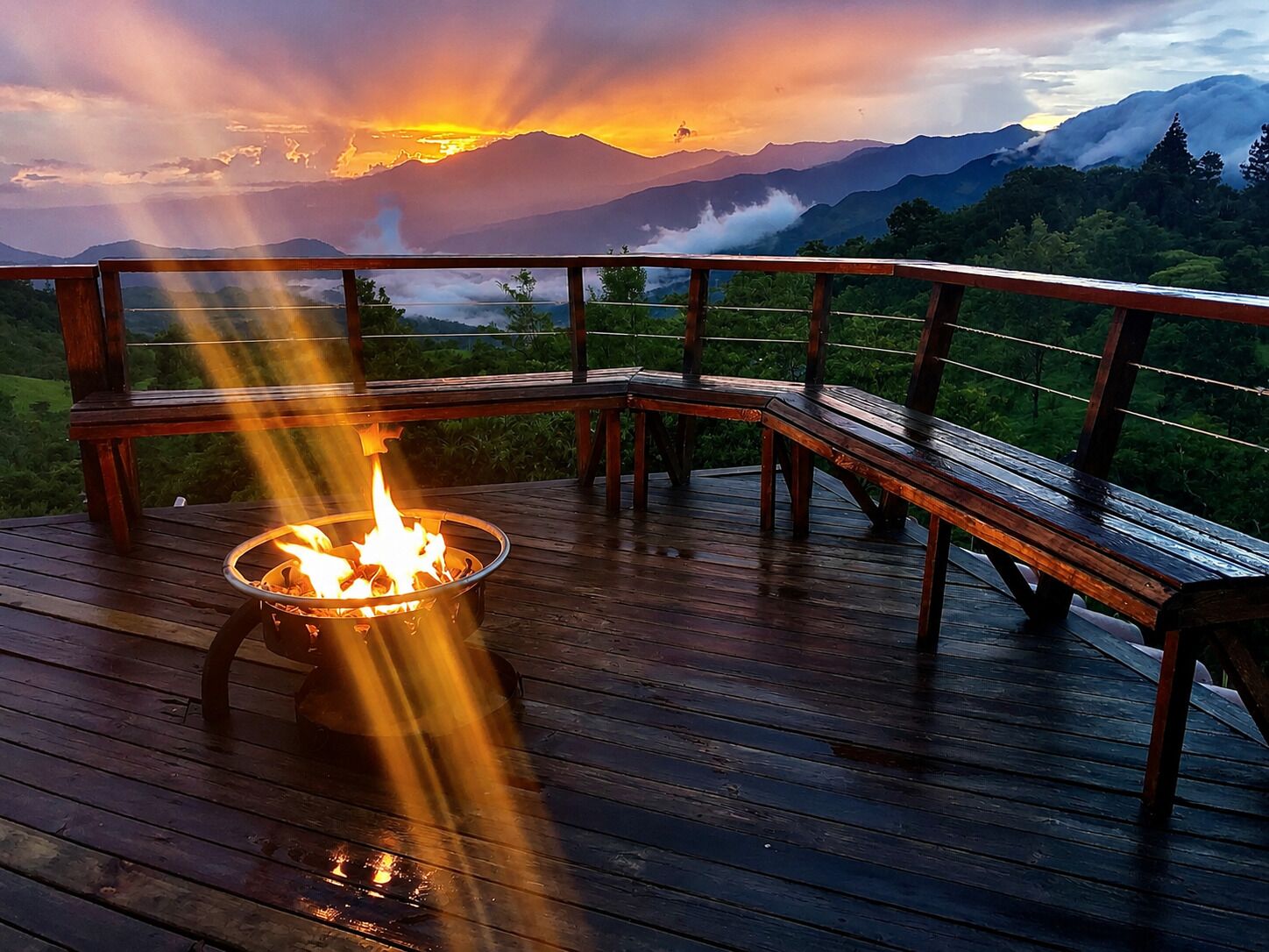 A wooden deck with a fire pit, overlooking a mountainous landscape at sunset.