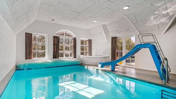 Une piscine intérieure avec un toboggan bleu, de grandes fenêtres et un plafond haut.