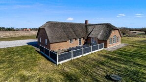 Une maison à toit de chaume, aux murs en briques, dotée d’un patio clôturé et d’une allée en gravier.