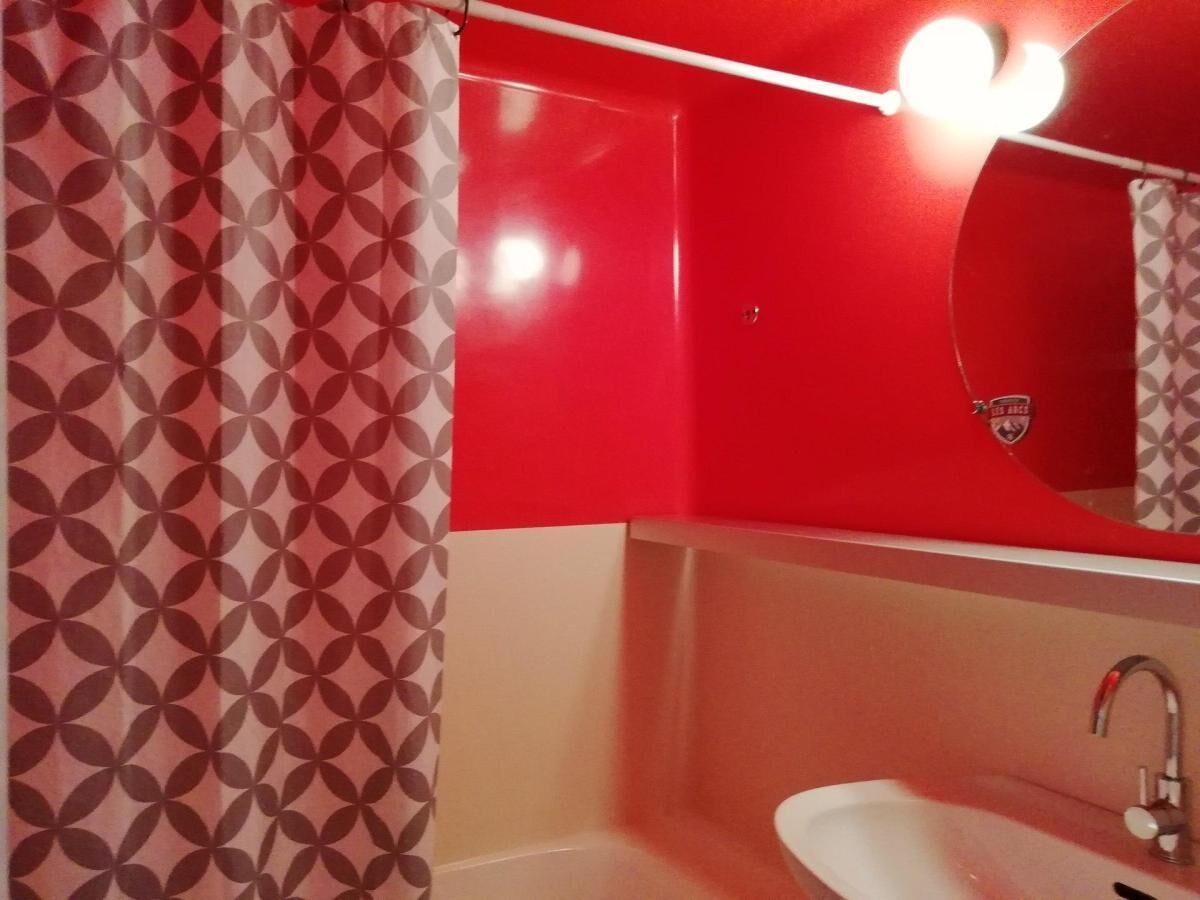 Un baño con un lavamanos rojo, un espejo y una cortina de ducha estampada.