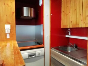 A compact kitchen with a dishwasher, stove, and sink, wooden cabinets, and a red wall. - 100m from ski slopes, 2nd floor, balcony, tv, ski locker, 28m², Les Arcs (Les Arcs)