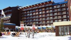Ein mehrstöckiges Hotel mit Balkonen, eine Skipiste im Vordergrund und ein klarer, blauer Himmel.
