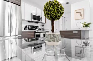 Una cocina moderna con electrodomésticos de acero inoxidable, una mesa de comedor de vidrio y una planta decorativa.