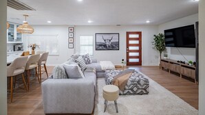 Un salon moderne avec un canapé, un pouf et un coin repas avec des chaises.