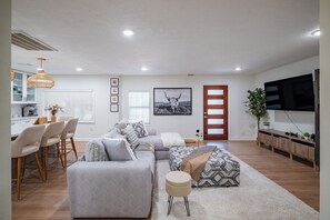 A modern living room with a sofa, ottoman, and dining area with chairs. - Modern Comfort: Spacious 6-Bedroom, 5-Bath Home (Houston)