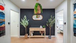 Un couloir avec une console en bois, des plantes en pot, un panier suspendu en osier contenant des plantes vertes et un miroir.