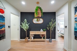 A hallway with a wooden console table, potted plants, a hanging wicker basket with greenery, and a mirror. - Modern Comfort: Spacious 6-Bedroom, 5-Bath Home (Houston)