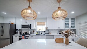 Une cuisine moderne avec des meubles blancs, un îlot central et deux suspensions en osier.