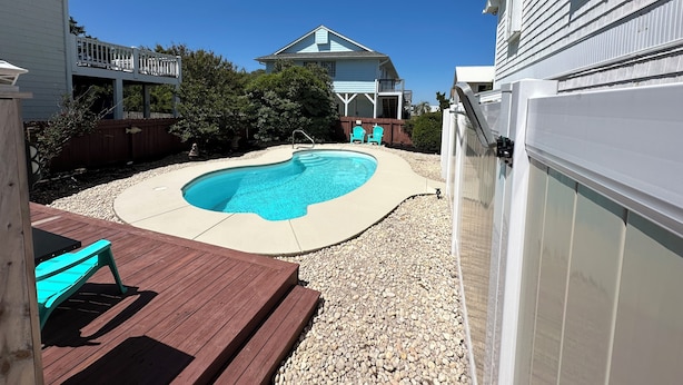 Ein Garten mit Swimmingpool, Holzterrasse und einem Haus im Hintergrund.