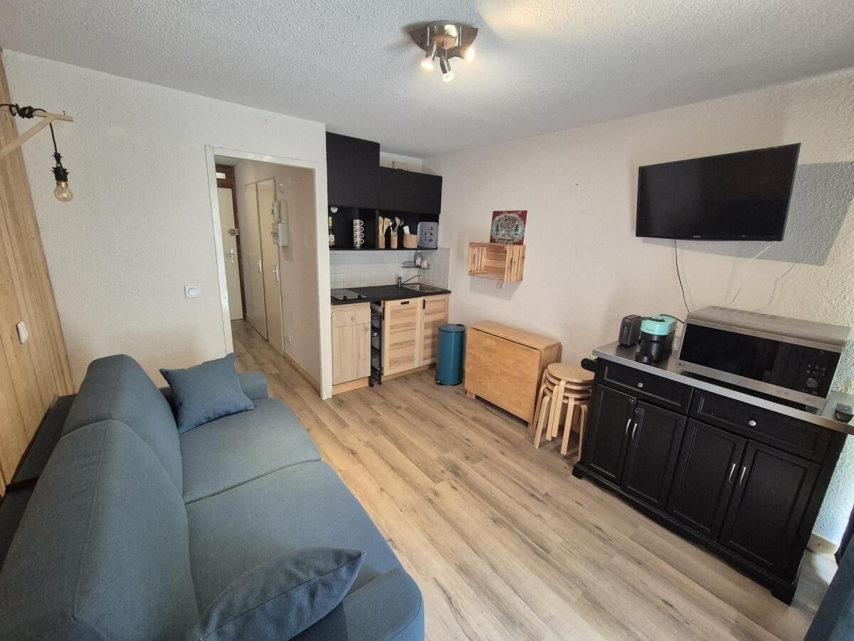 A compact living space with a sofa, kitchenette, and a flat-screen TV mounted on the wall.
