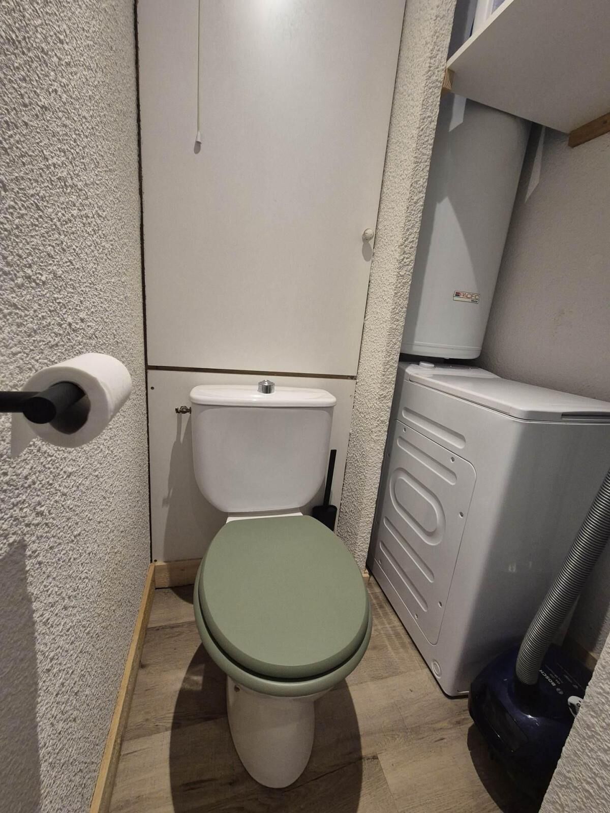 A small bathroom with a toilet, a hand dryer, and a vacuum cleaner.