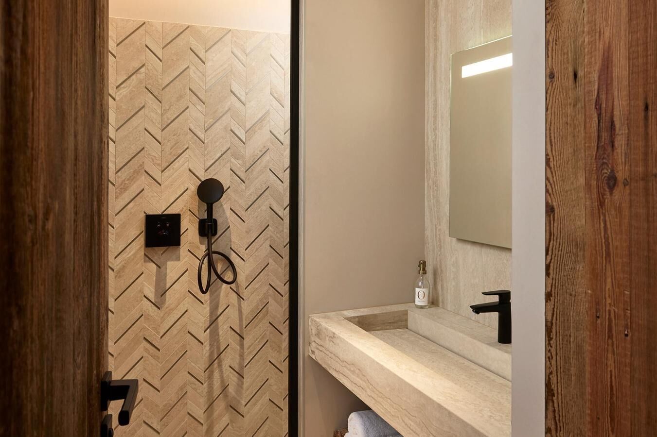 A bathroom with a herringbone-patterned wall, a shower with a handheld showerhead, a sink with a mirror, and a towel rack.