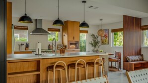 A modern kitchen with wooden bar stools, pendant lighting, and a large island. - Casa Tranquila • Pool, Ping Pong, Game Room & More (Austin)