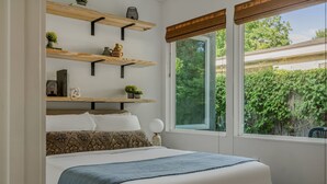 A bedroom with a bed, a window with a view of greenery, and wooden shelves with decorative items. - Casa Tranquila • Pool, Ping Pong, Game Room & More (Austin)