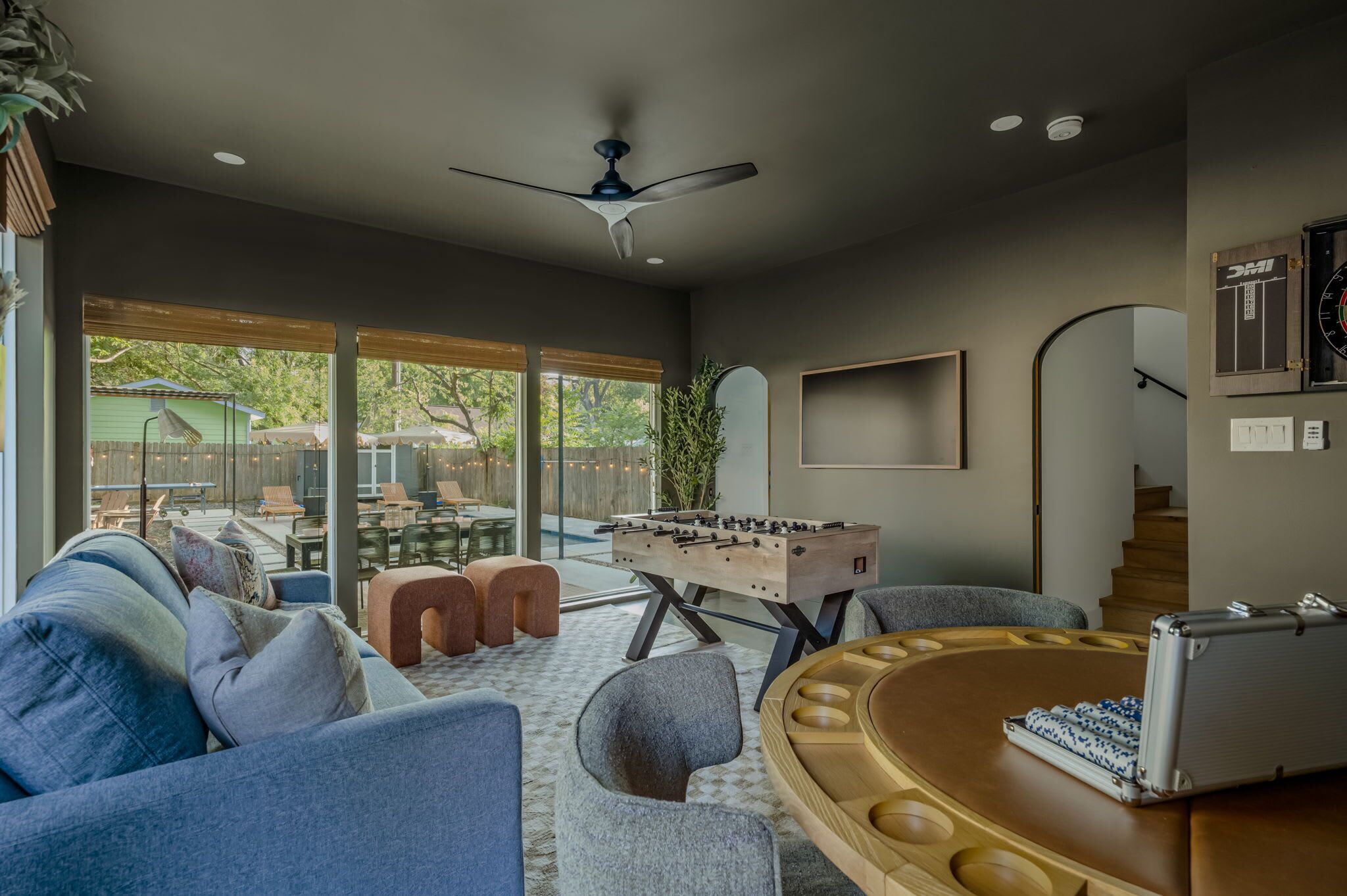 A modern living room with a foosball table, comfortable seating, and a large window overlooking a backyard.