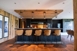 Eine moderne Küche mit Holzbalkendecke, einer zentralen Kochinsel mit Barhocker und einem Essbereich mit Stühlen.