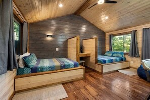 Ein Blockhaus-Innenraum mit Schlafkoje oben, einer unteren Schlafgelegenheit und einem kleinen Schreibtisch.