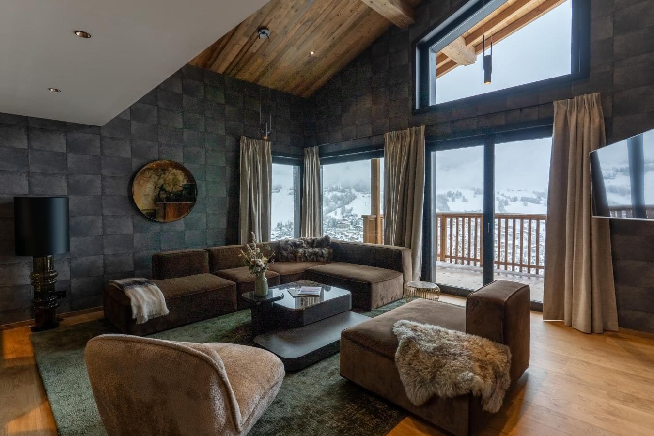 A modern living room with a stone wall, a large window with a view, and a wooden ceiling.