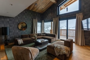 A modern living room with a stone wall, a large window with a view, and a wooden ceiling. - View village, parking, ski locker, 220m², Megève (Megève)