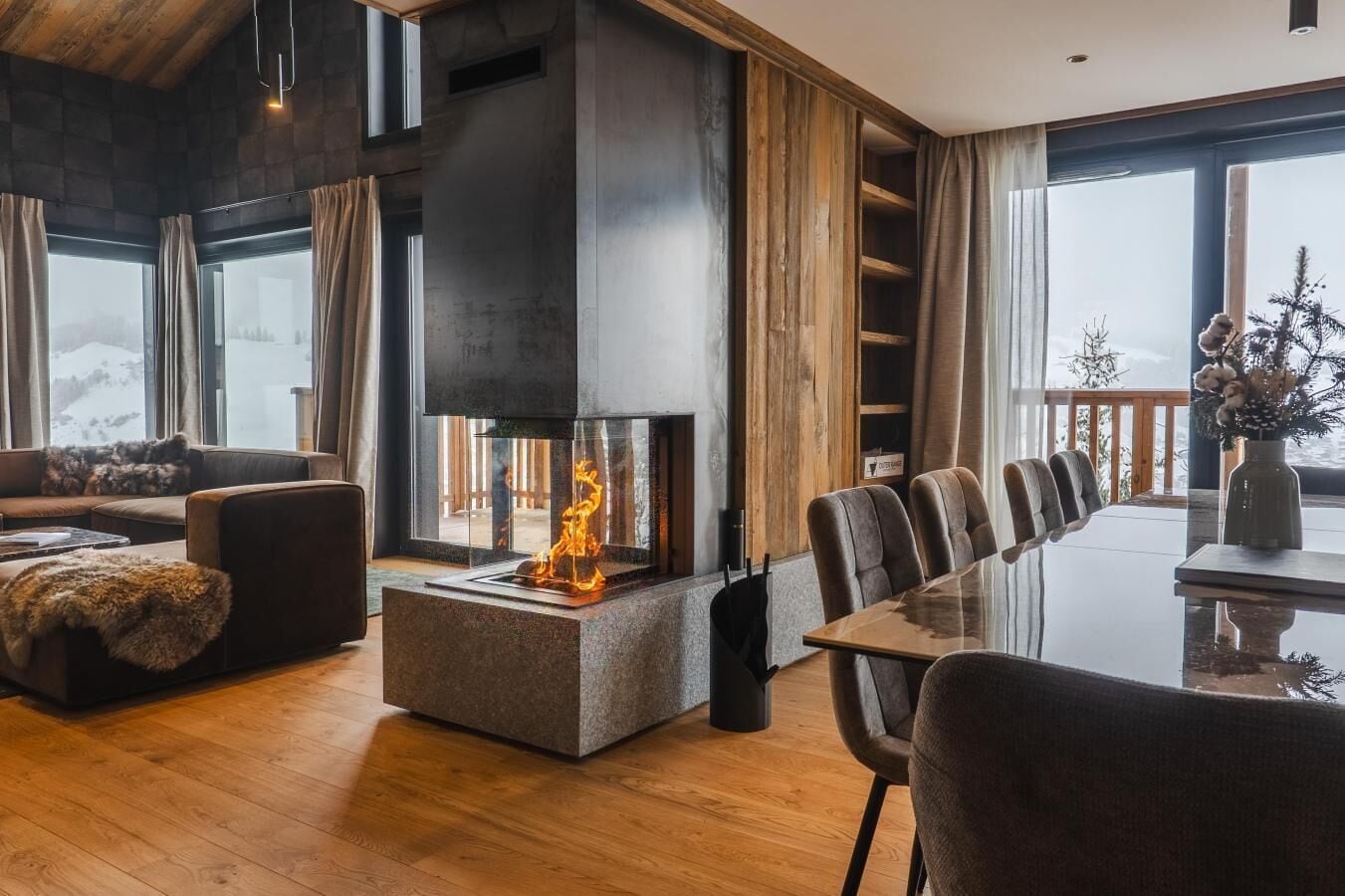 A modern living room with a fireplace, a sofa, a dining table with chairs, and large windows.