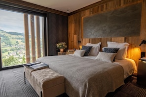 A modern bedroom with a large bed, a bench, a view of the countryside, and wooden paneling. - View village, parking, ski locker, 220m², Megève (Megève)