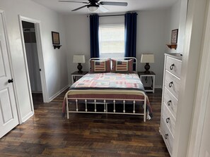 Un dormitorio con cama, dos mesitas de noche, cómoda y ventilador de techo, además de una ventana con cortinas.