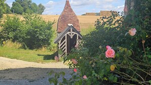 Un cadre rural avec un petit bâtiment, un chemin de gravier et des rosiers en fleurs.