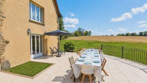 Une terrasse avec une table dressée pour les repas, un espace salon abrité et une vue sur la campagne.