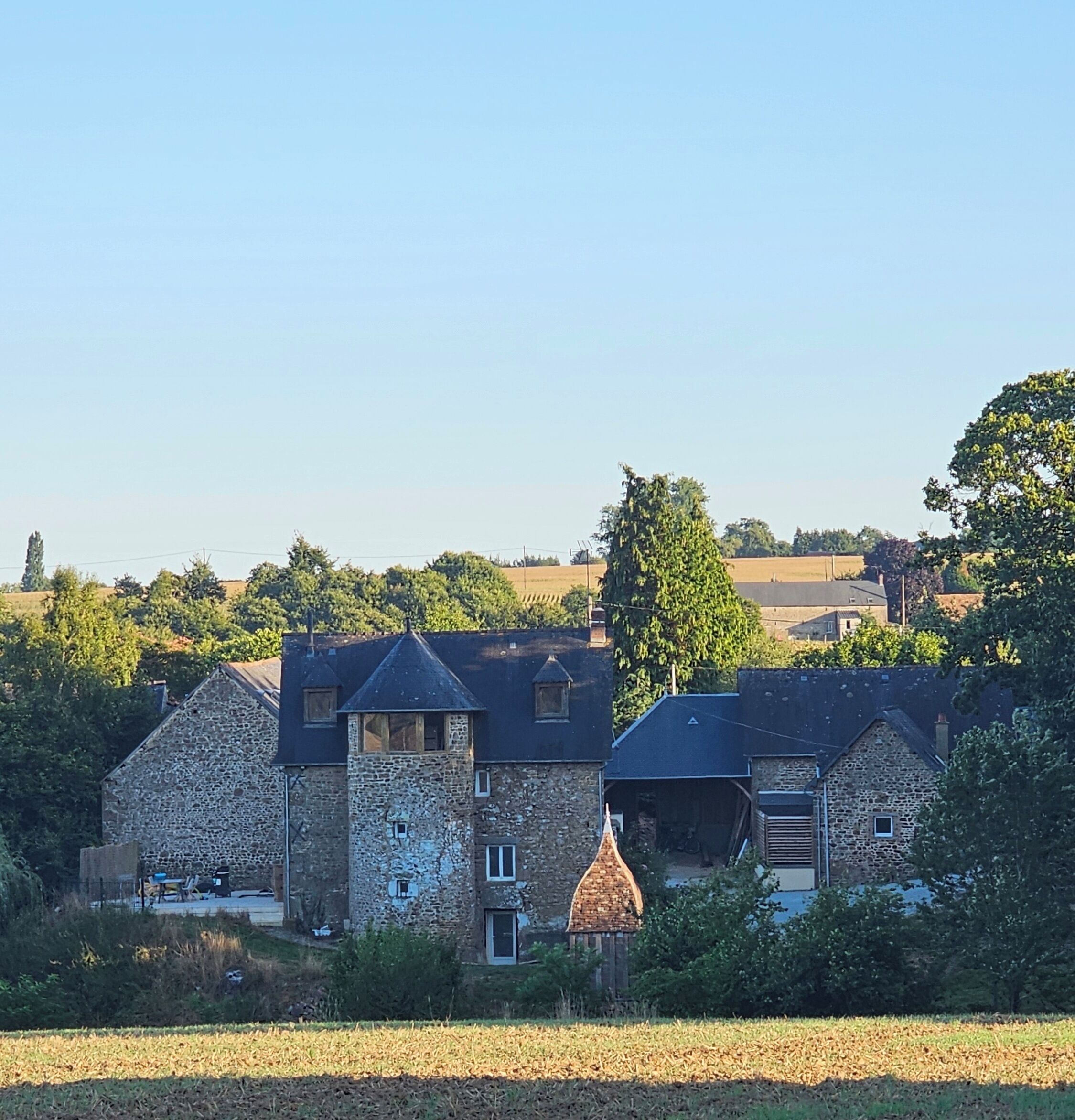 Un bâtiment en pierre doté de plusieurs cheminées, d’une petite tour et d’une porte.